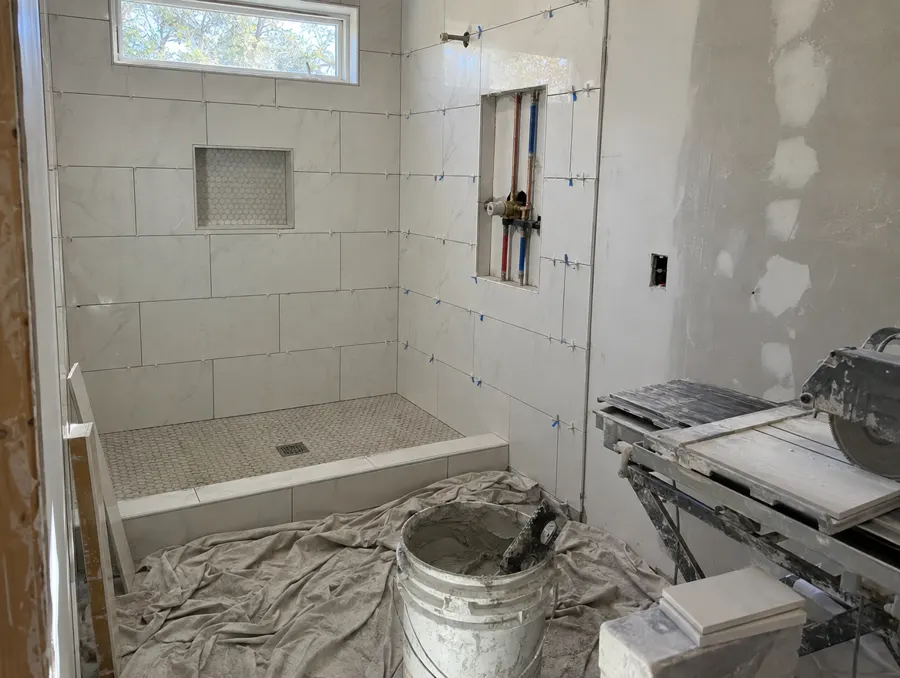 A shower mid-remodel with new white tile and the valve plumbing showing in the wall